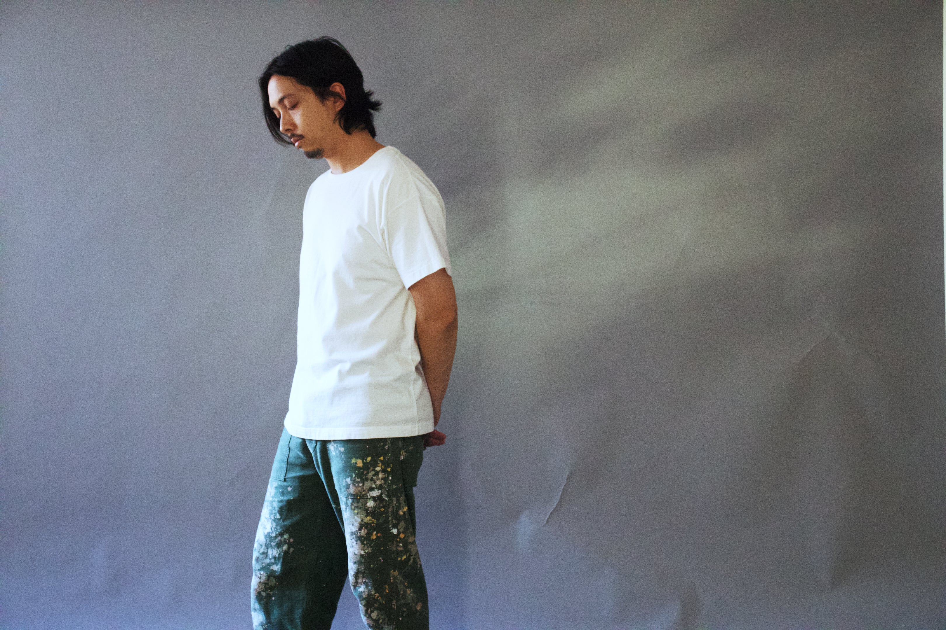 Person wearing a white t-shirt and green pants against a plain background
